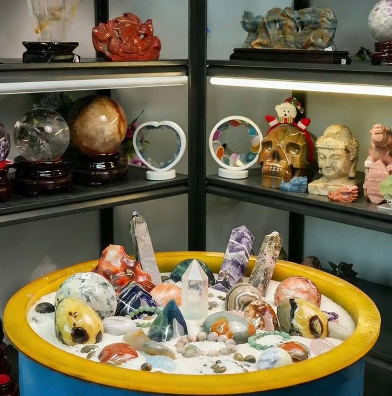Collection of crystals and figurines on shelves with a bowl of crystals in the foreground.