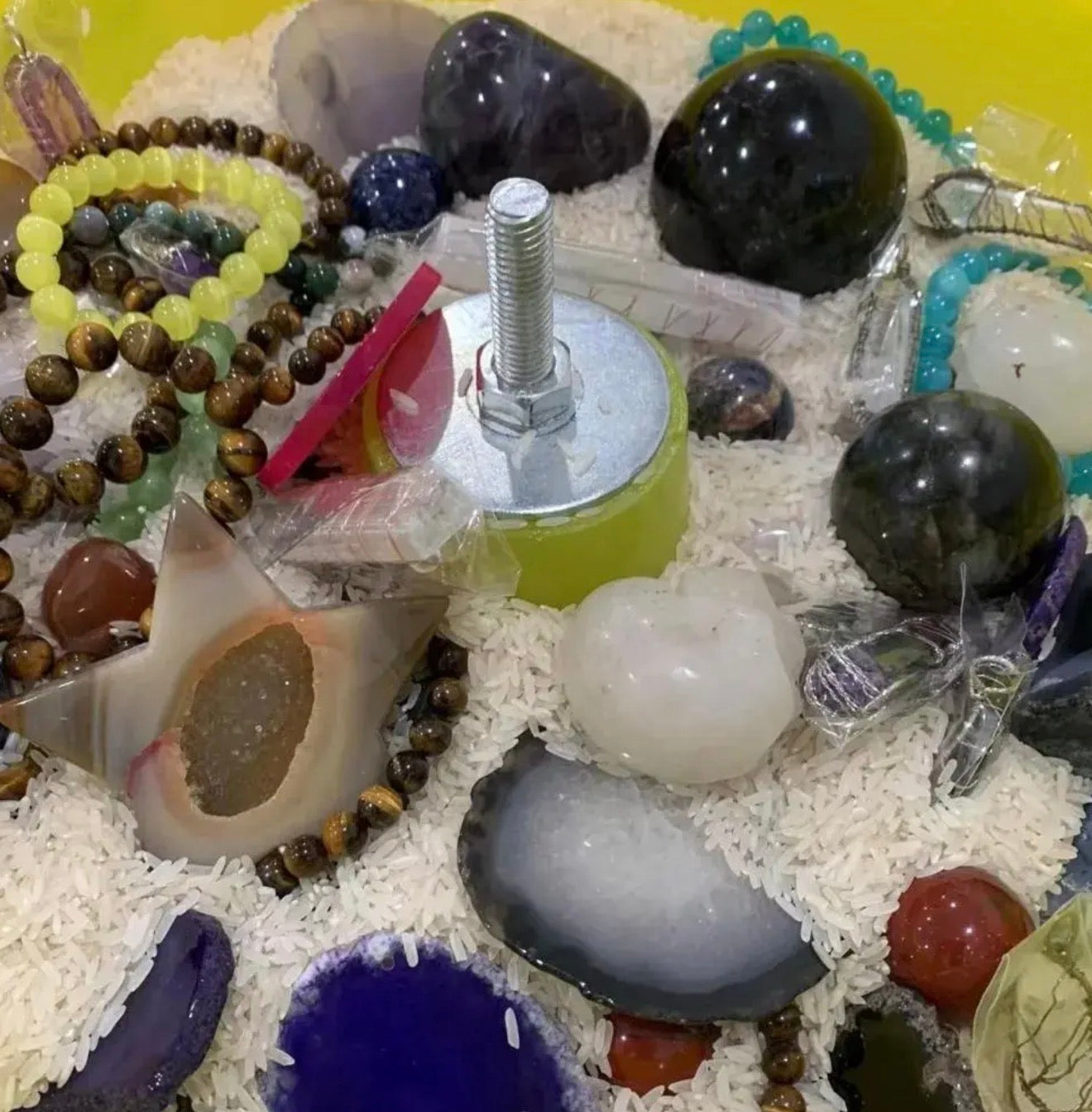 Collection of stones, crystals, and a bolt on a white surface with a yellow background